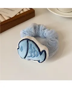 Close-up of fluffy blue plush hair scrunchie with cute embroidered fish charm detail