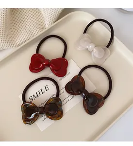 Close-up of four bow-knot hair ties in red, white, and tortoiseshell on a cream tray