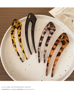 Close-up of four colorful U-shaped hair pins with gold logos on a ceramic plate