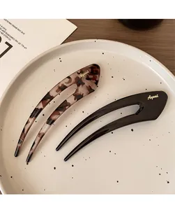 Close-up of elegant tortoise shell and black U-shaped hair forks with gold logo lettering