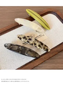Close-up of four acetate spring hair clips in marble and solid colors on a wooden tray