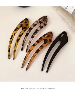 Macro detail of tortoiseshell and black U-shaped hair forks with golden brand lettering
