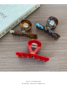 Three acetate hair claws in red and tortoiseshell finishes shown on a wooden desk