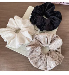 Detailed close-up of velvet scrunchies in white, black and brown on a wooden surface