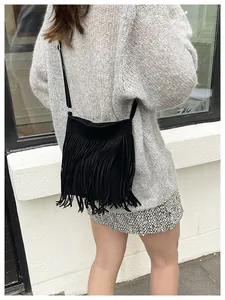Detail of black suede shoulder bag with long fringes shown on model for boho chic style