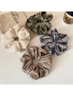 Detailed close-up of velvet hair scrunchies in olive, beige, grey, and light brown colors