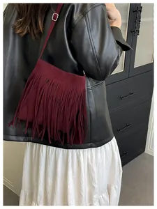 Detail of burgundy fringe crossbody bag featuring suede texture and silver metal buckle