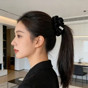 Elegant black velvet scrunchie for ponytails with a decorative silver rectangular label