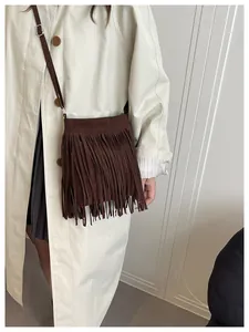 Detailed view of deep brown fringed crossbody bag on beige trench coat for autumn style
