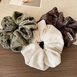 Three plush oversized scrunchies in green, beige, and coffee on a wooden desk