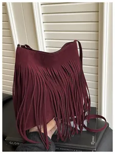 Detail of burgundy fringe crossbody bag with suede texture on a minimalist backdrop