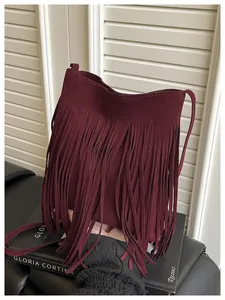 Detail of burgundy fringe crossbody bag in suede finish on elegant bookshelf setting