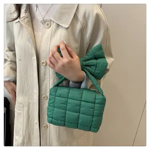 Detail of green quilted shoulder bag with large decorative bow on handle and silver zipper