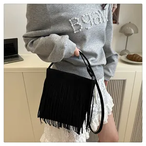 Détail du sac à bandoulière en daim noir avec franges denses sur un bureau élégant