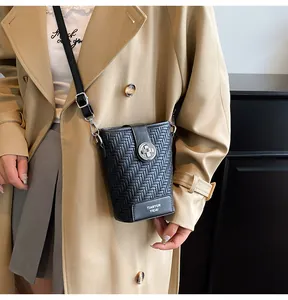 Detail van zwarte geweven telefoontas met zilveren gesp gedragen op een beige trenchcoat