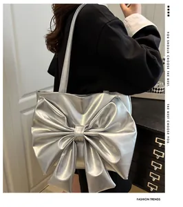 Detail of silver metallic tote bag with large bow and thin shoulder straps worn by model