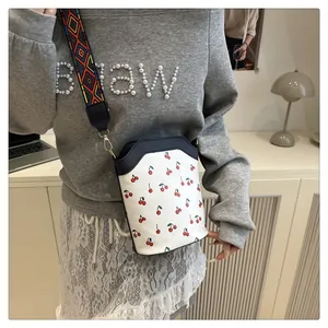 Detail of white bucket bag with cherry print and colorful geometric woven strap