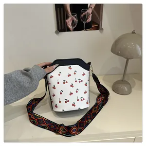 Detail van de witte bucketbag met kersenprint en een kleurrijke geometrische schouderband