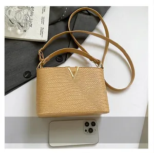 Bolso bandolera tejido caqui con hebilla en V dorada y un smartphone para comparar tamaño