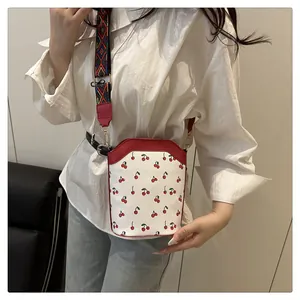 Detailed view of white leather cherry print bucket bag with ethnic style wide strap