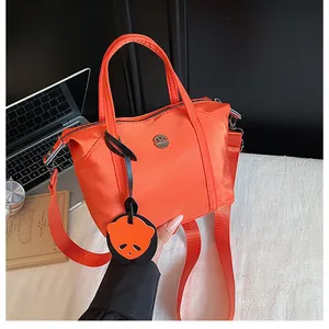 Détail du sac orange en nylon avec pendentif panda et large bandoulière réglable
