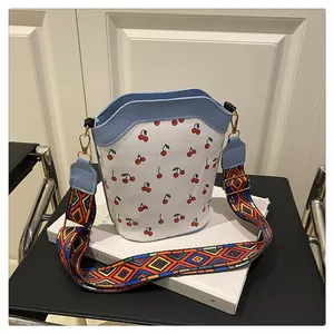 Detailed view of bucket bag with red cherry print and colorful geometric woven strap