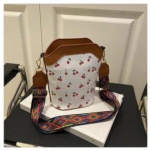Detail of white cherry print bucket bag with brown leather trim and retro woven strap