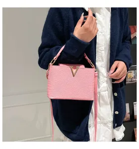 Close-up of pink crossbody bag with metal V-buckle on a blue knitted cardigan