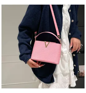 Sac à main rose en cuir tressé avec boucle en V dorée, porté par un mannequin élégant