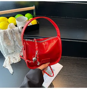 Detail of red glossy PU leather handbag with gold chain strap and metal ball charm