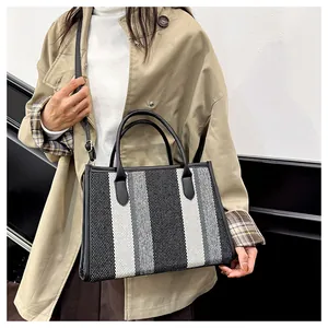 Close-up of striped canvas tote bag with black leather handles and detachable strap
