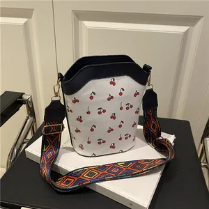 White cherry print bucket bag with colorful wide shoulder strap on a book background