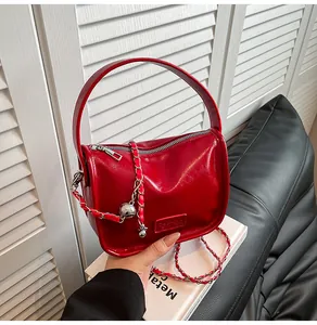 Detail of glossy red handbag featuring a silver chain strap with decorative metal ball