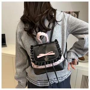Detail eines schwarzen Lederrucksacks mit rosa Rüschenbesatz und süßem Schleifenanhänger