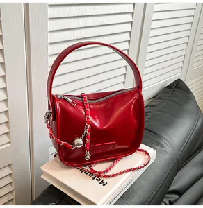 Detail of red patent leather shoulder bag with metallic chain and embossed fashion logo