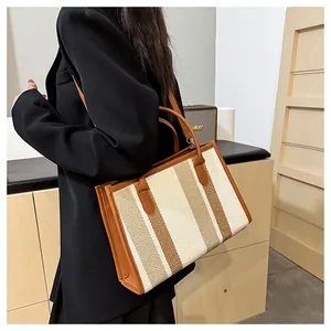Close-up of stylish striped canvas tote bag with brown leather handles worn by model