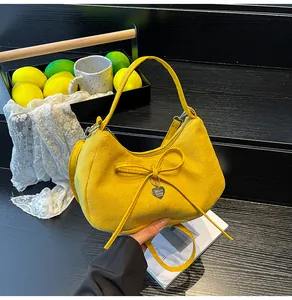 Detail of yellow crescent suede tote bag with heart pendant and bow on black stairs
