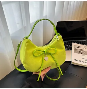 Detail of green crescent tote bag with bow accent and heart pendant on a desk