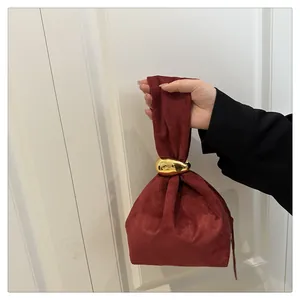 Detail of burgundy suede bucket bag featuring a large polished golden bean metal handle