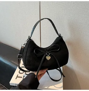Detail of black suede tote bag featuring a bow, golden heart pendant and shoulder strap