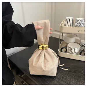 Detail of beige suede handbag with a large gold metal ring handle on a black wood table