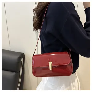 Detail of red patent leather shoulder bag with gold clasp shown on a model