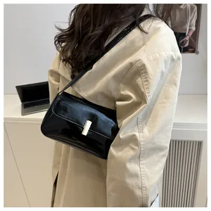 Detail view of black patent leather shoulder bag with sleek gold metallic buckle