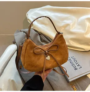 Detail of brown faux suede tote bag featuring a bow and metal heart charm on the strap