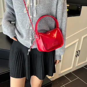 Glossy red crossbody bag with chain strap and top handle for women in a stylish pose