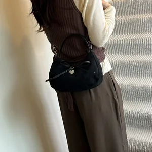 Large black suede crescent tote bag with heart pendant and bow detail on model