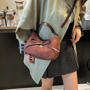 Brown faux suede tote bag with heart charm and bow, shown on model in a cozy cafe setting