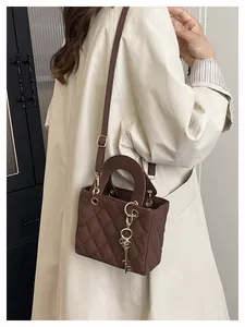 Close-up of brown quilted leather texture and gold key charm on square handbag