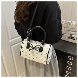 Detail of white textured barrel bag with black bow prints and heart charm on a model