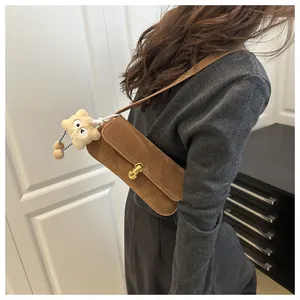 Detail of brown suede shoulder bag with gold metal clasp and plush bear charm decoration